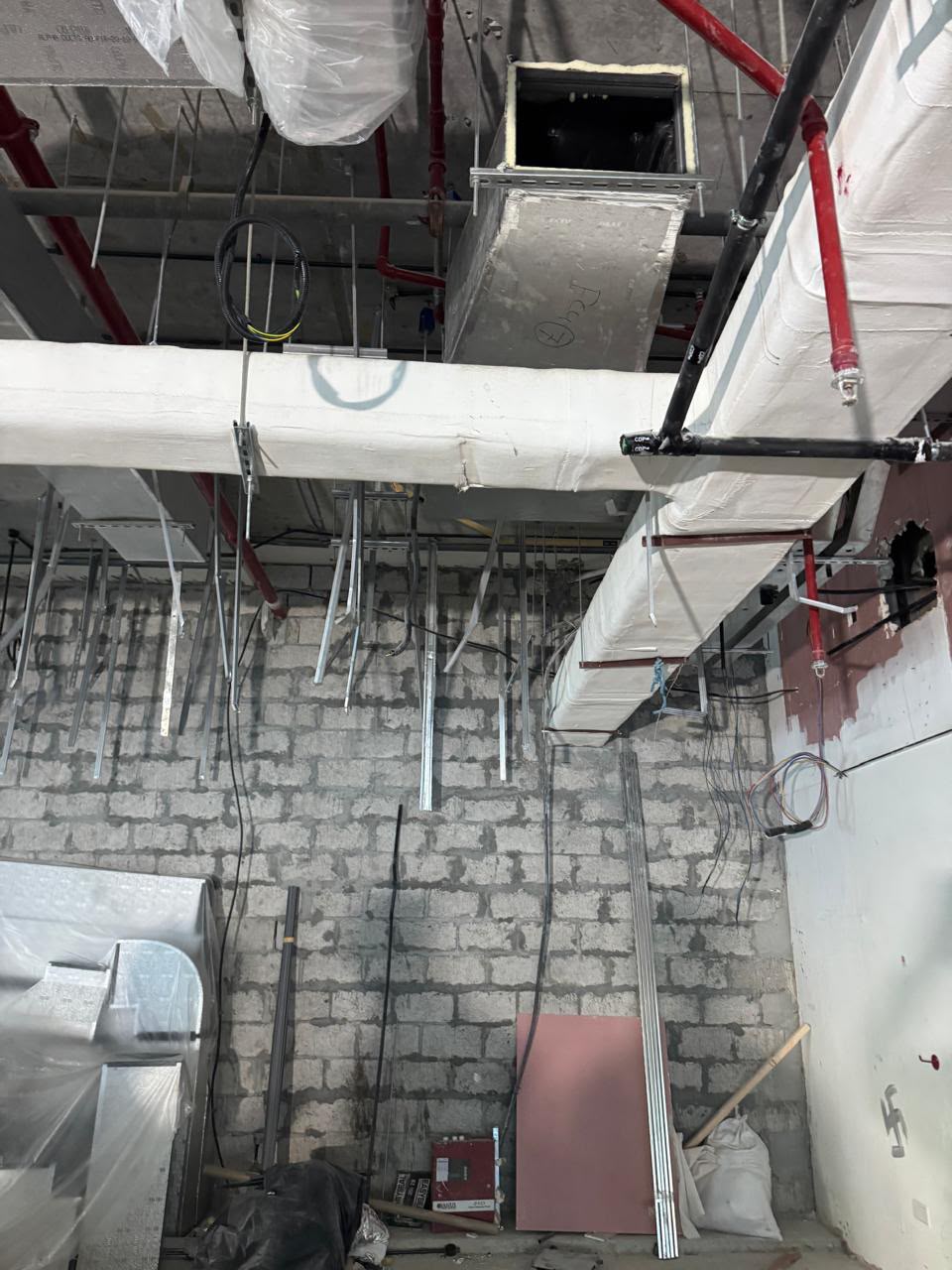 Overhead view of insulated ductwork and MEP cabling installed above a masonry ceiling