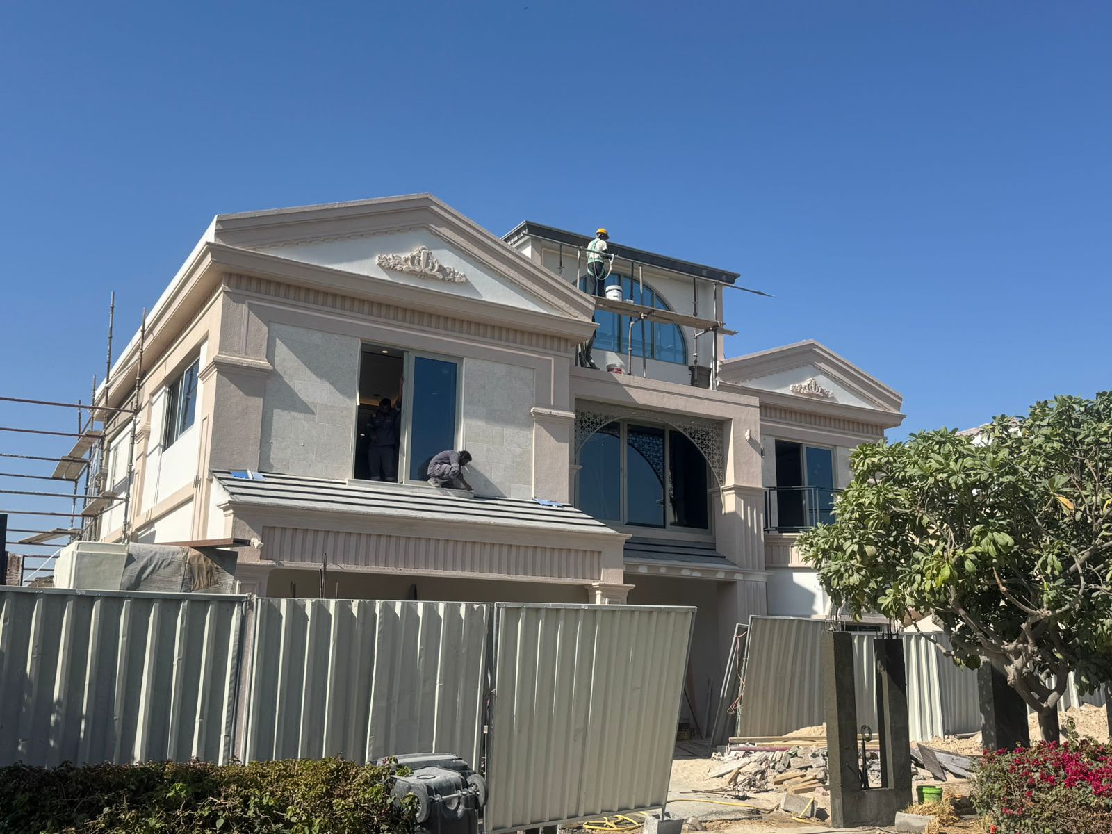 Two-story villa exterior with workers finishing the roof and facade